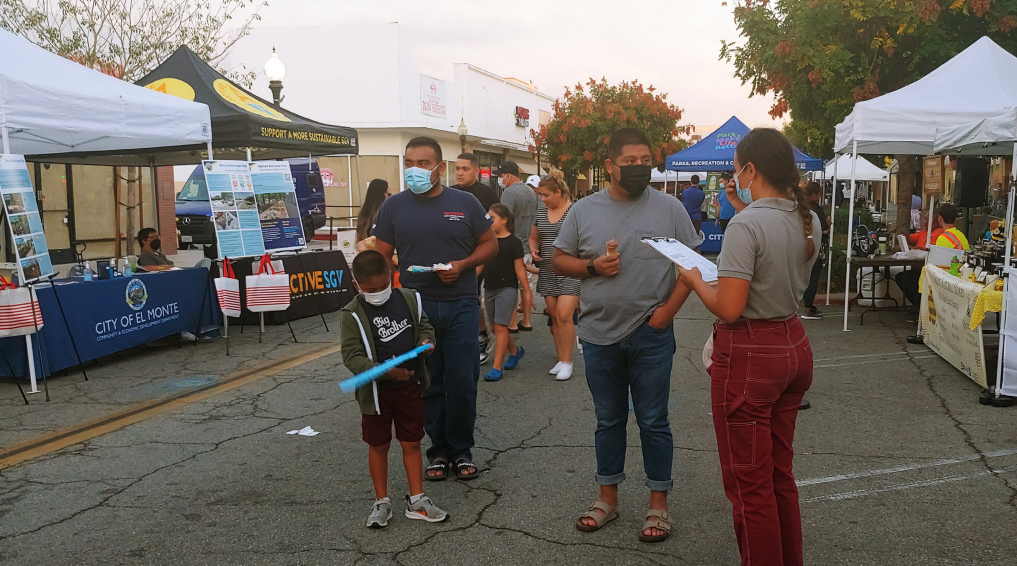 Street fair with people interacting and booths on both sides.