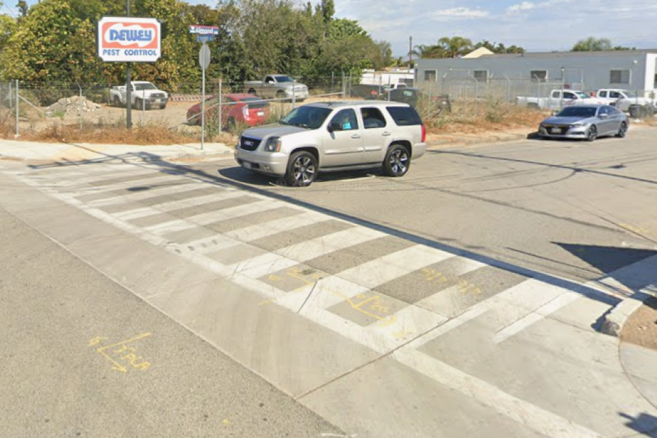 Intersection with a crosswalk, cars and distant buildings under a clear sky.