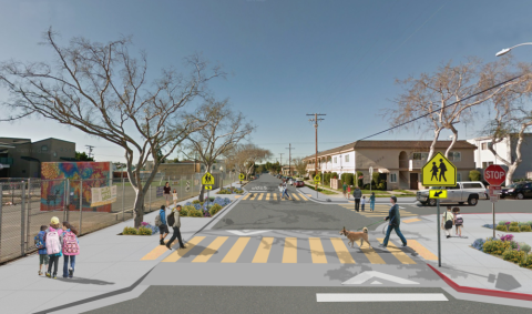 Street with crosswalk, people walking, bare trees, and clear sky.