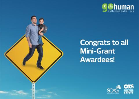 A man holding a child on a pedestrian crossing sign against a blue sky.